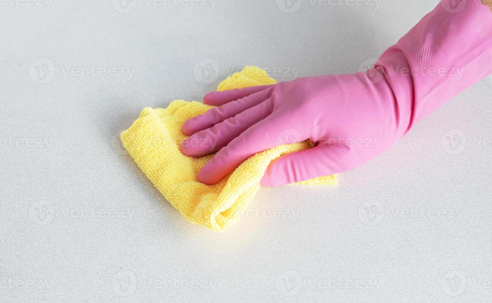 uma mão dentro uma Rosa luva lenços a superfície com amarelo microfibra. Alto qualidade foto