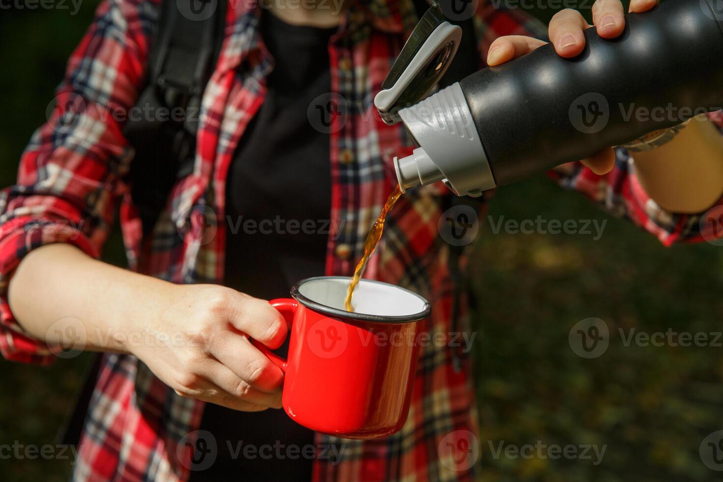 turista mãos derramar café a partir de uma garrafa térmica para dentro uma metal vermelho xícara.seletiva foco. fundo borrado. Alto qualidade foto