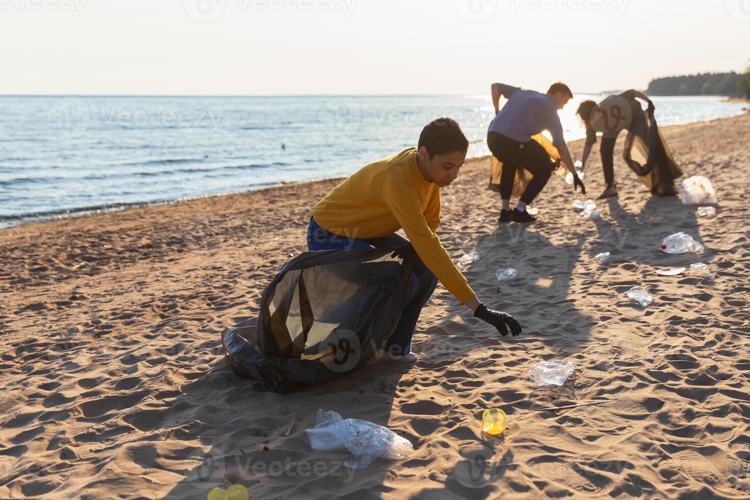 terra dia. voluntários ativistas coleta lixo limpeza do de praia costeiro zona. mulher e mans coloca plástico Lixo dentro lixo saco em oceano costa. de Meio Ambiente conservação costeiro zona limpeza foto