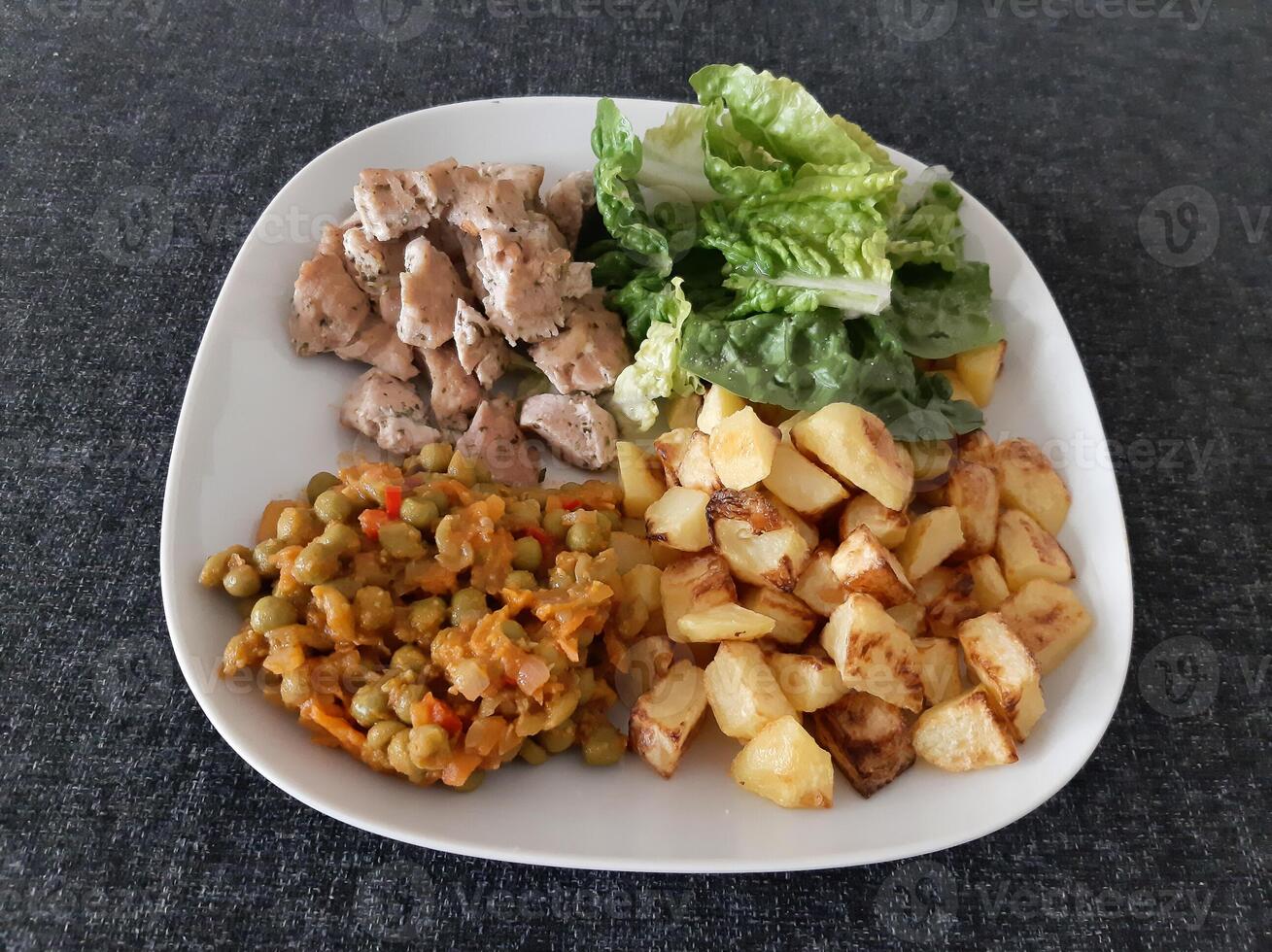 caseiro grelhado frango com francês fritas, verde salada e ervilha ensopado servido em uma branco prato foto