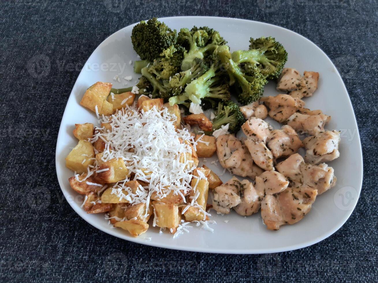 caseiro grelhado frango com francês fritas, queijo e brócolis, servido em uma branco prato foto