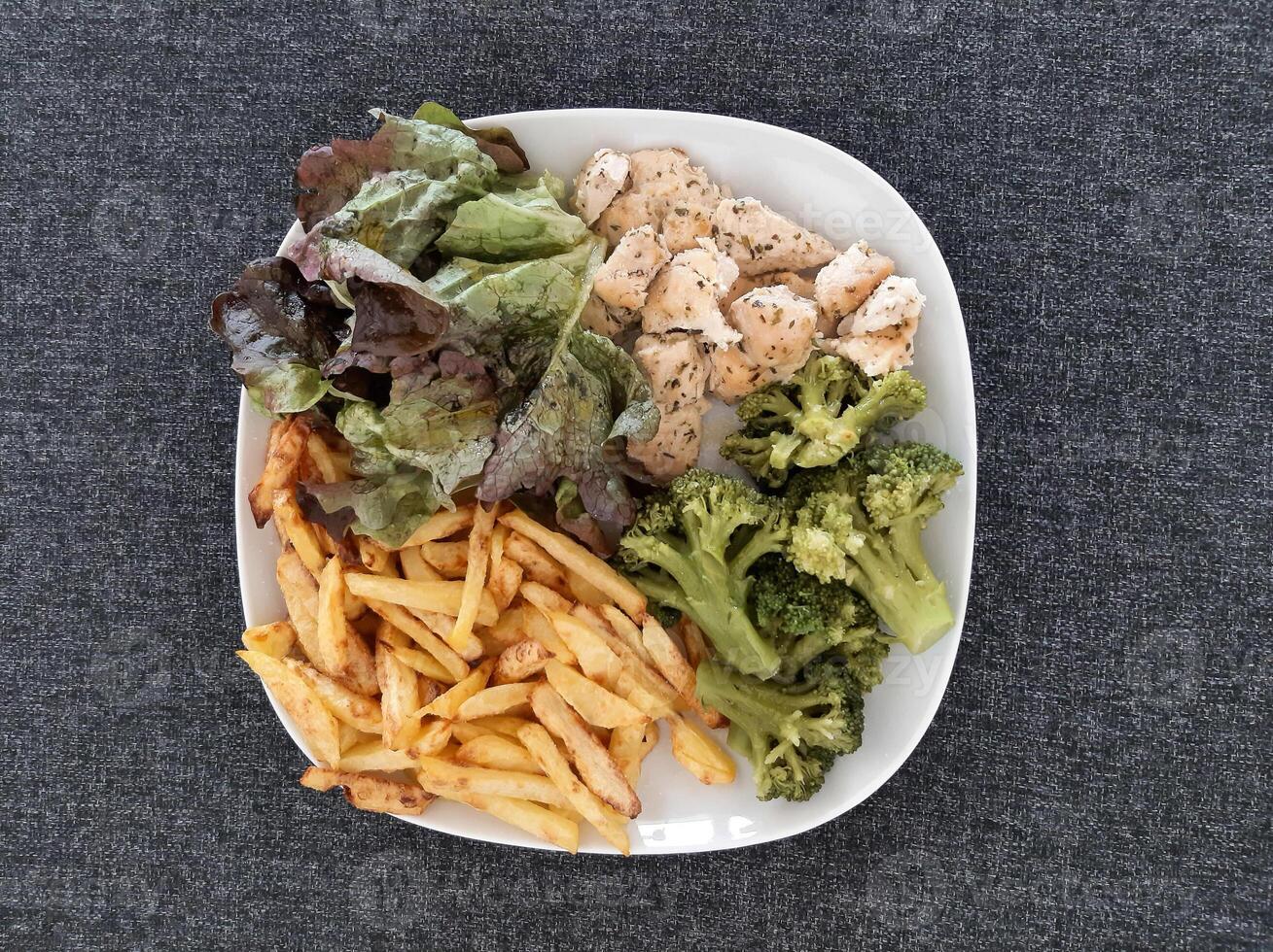 caseiro grelhado frango com francês fritas, brócolis e verde salada, servido em uma branco prato foto