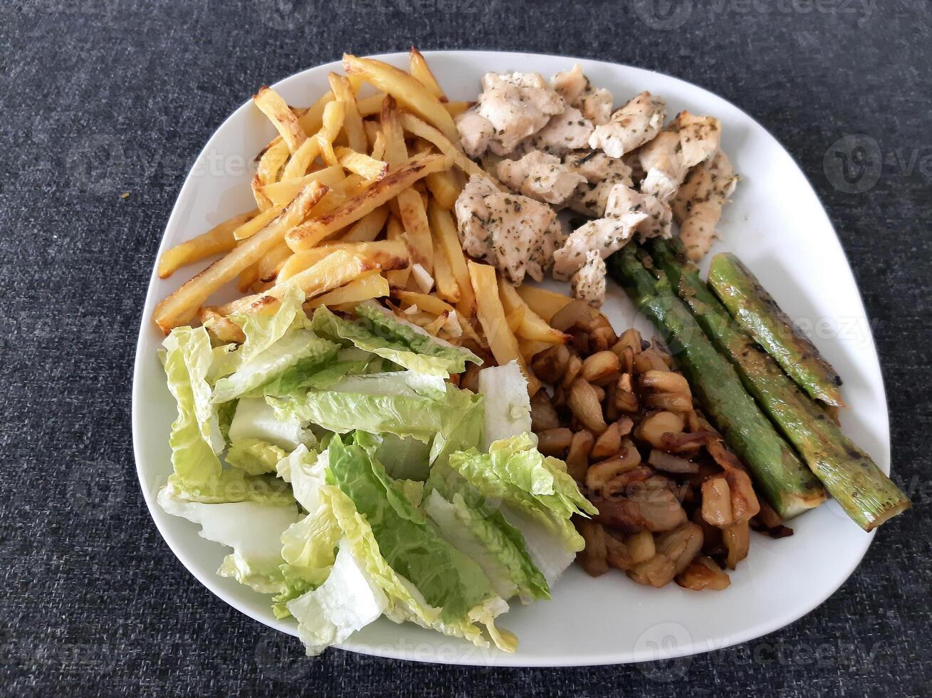 caseiro grelhado frango com francês fritas, espargos, grelhado picado Berinjela e verde salada, servido em uma branco prato foto