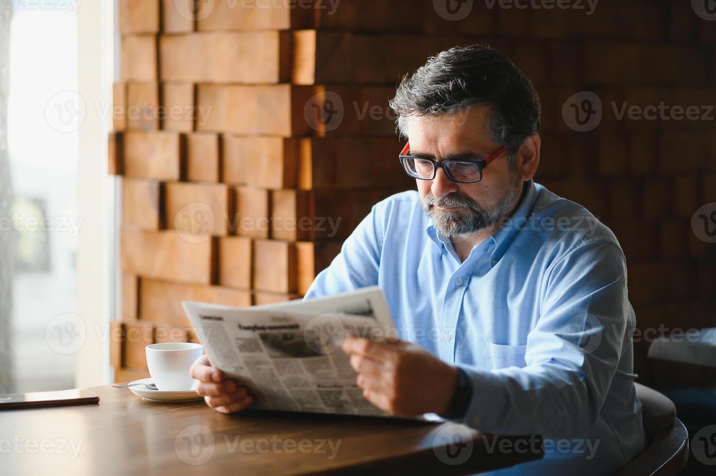 ativo Senior homem lendo jornal e bebendo café dentro restaurante foto