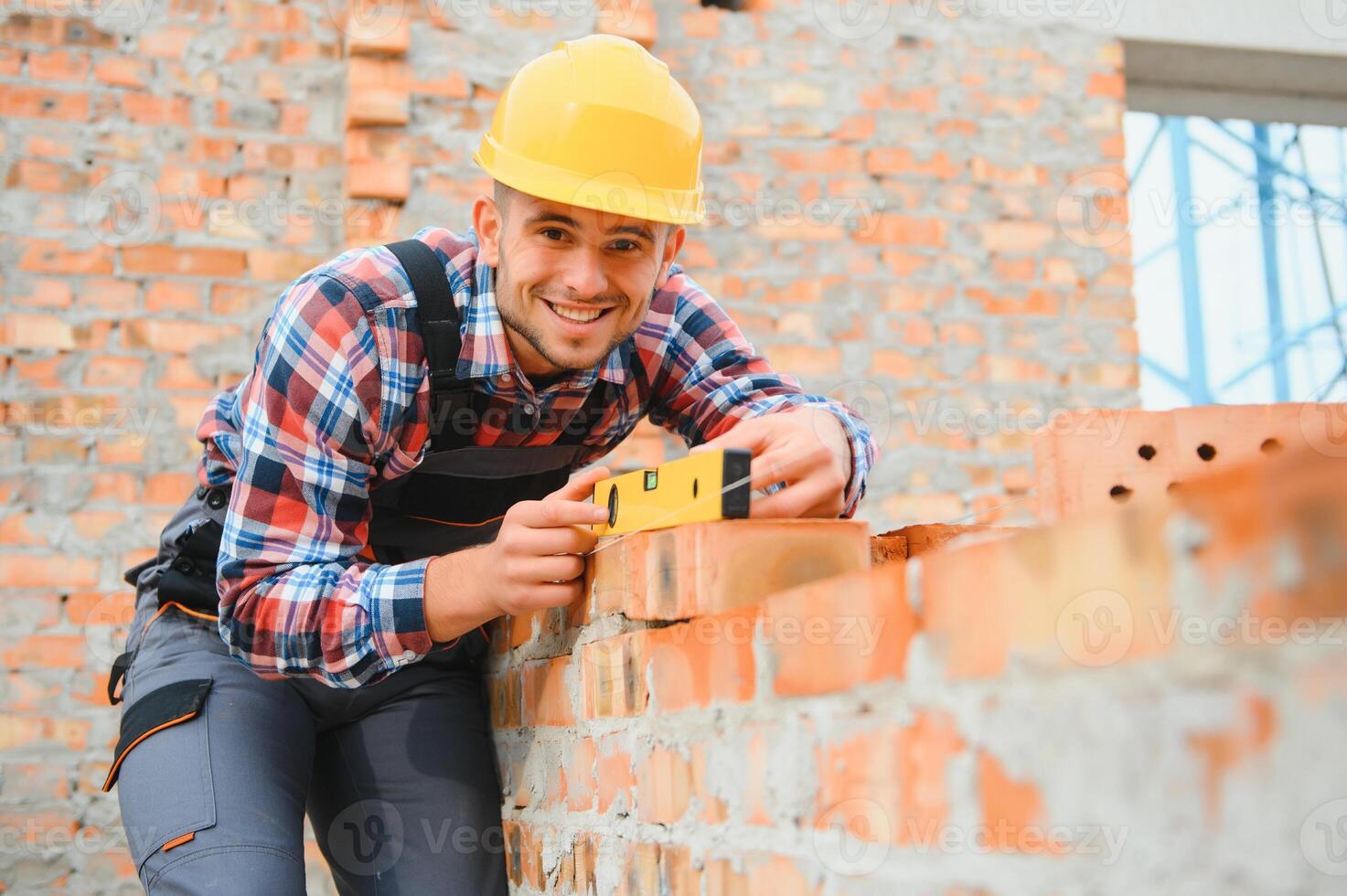 usando tijolos. jovem trabalhador da construção civil de uniforme está ocupado no prédio inacabado foto