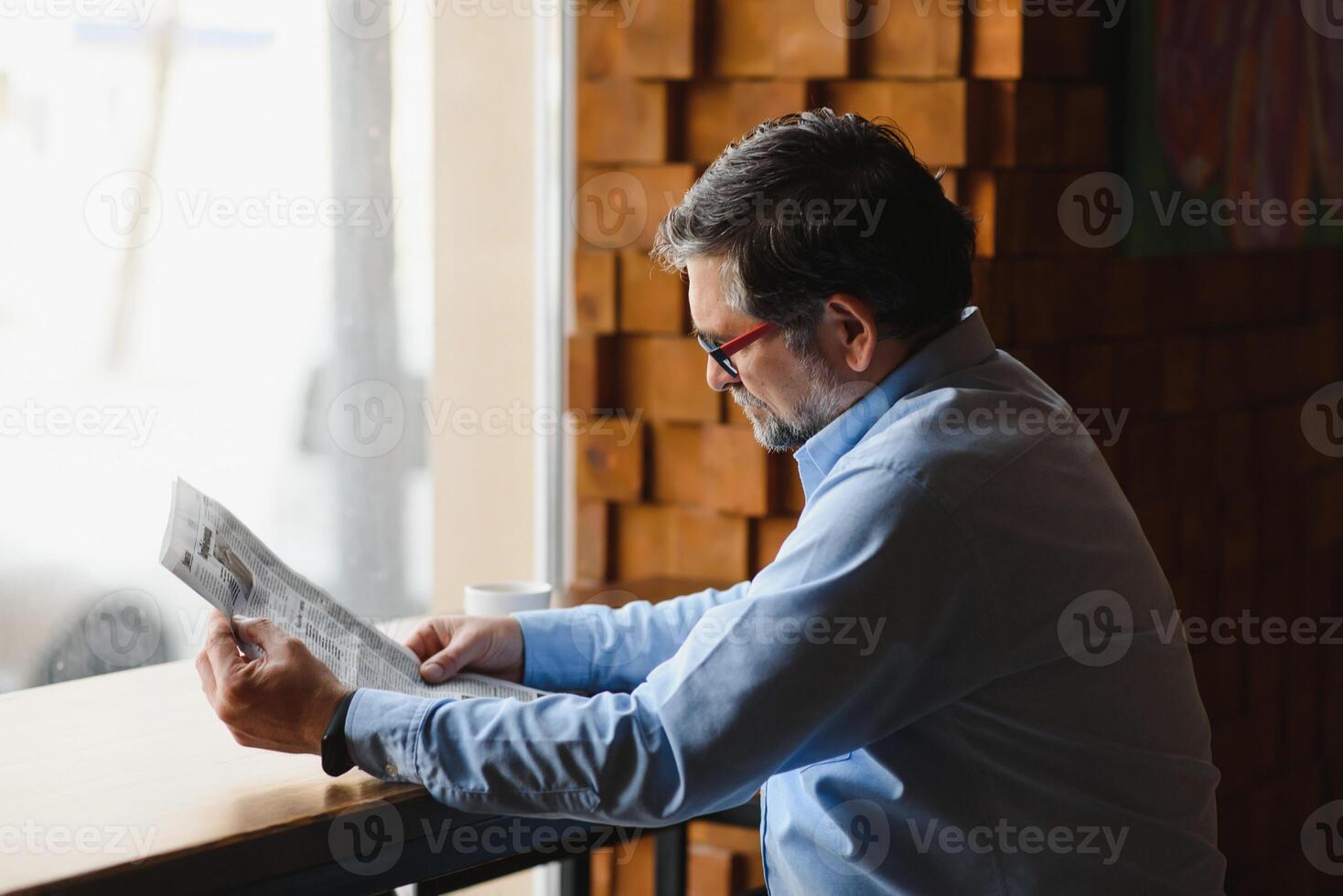 ativo Senior homem lendo jornal e bebendo café dentro restaurante foto