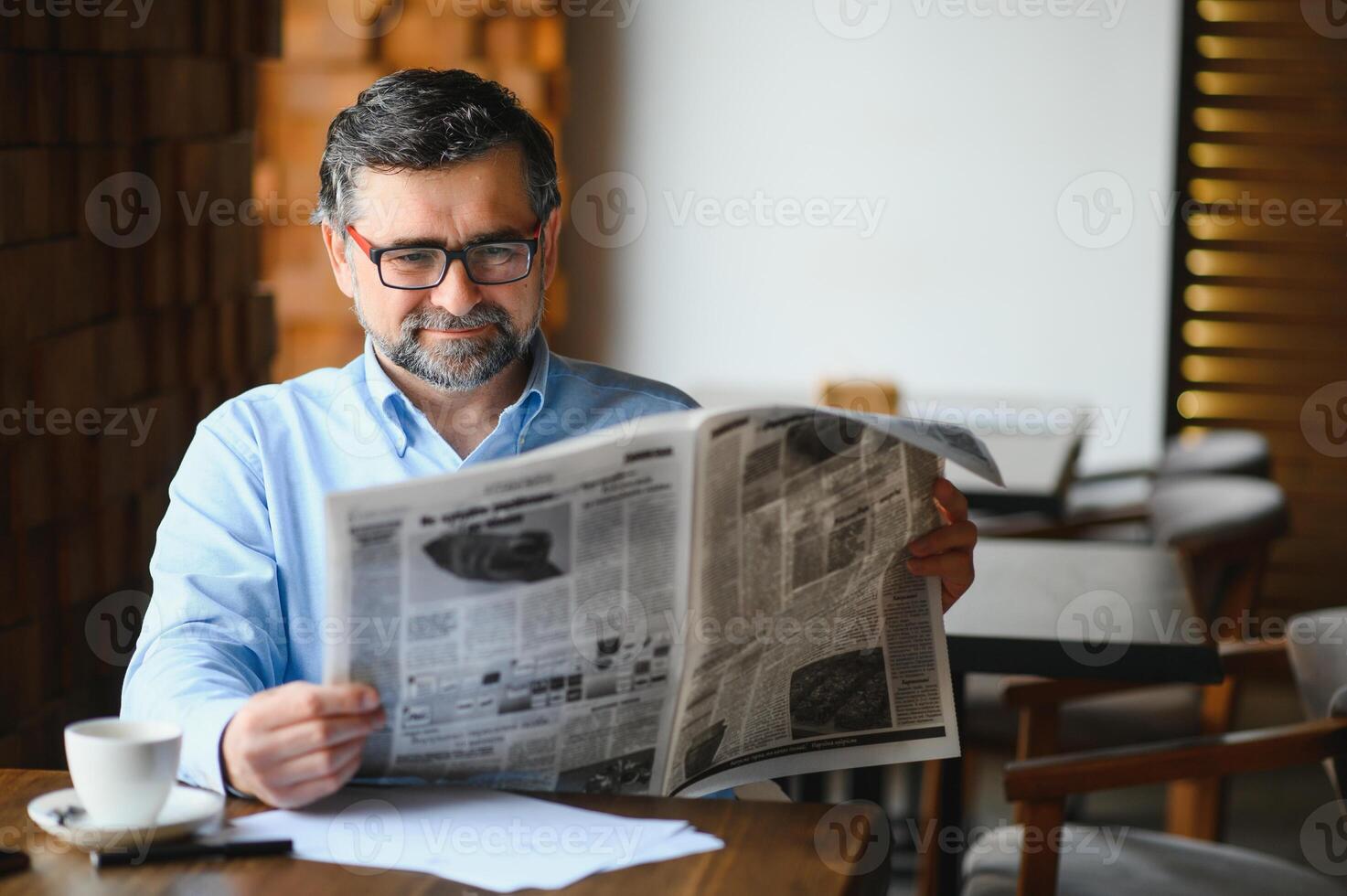 ativo Senior homem lendo jornal e bebendo café dentro restaurante foto