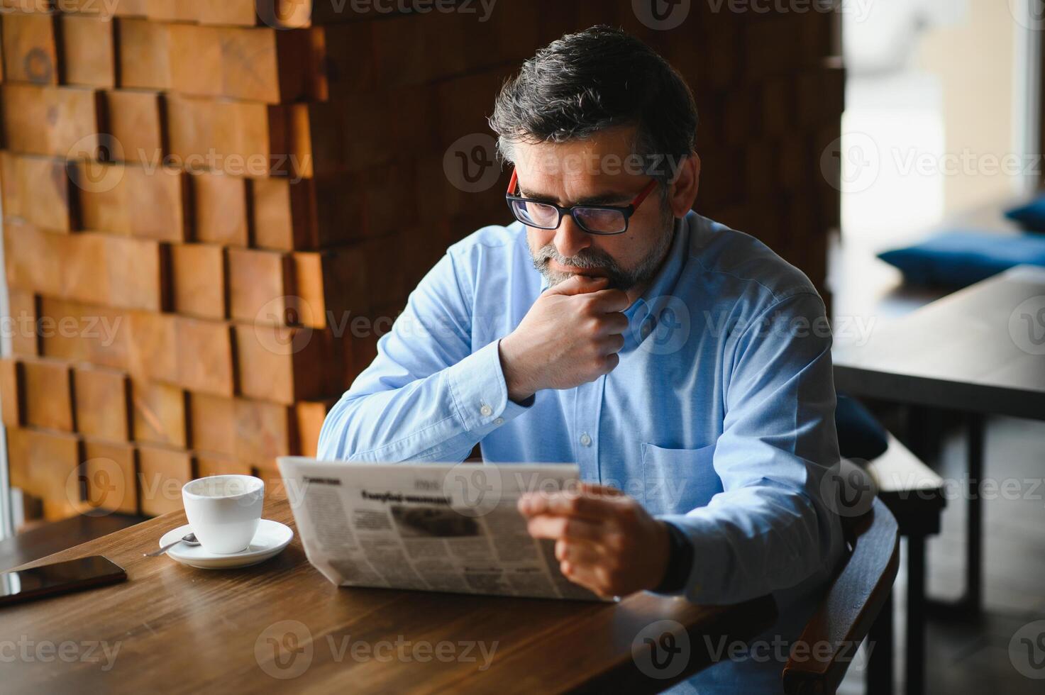 fechar-se retrato do sério Senior bonito homem lendo jornal, tendo café pausa e sentado às mesa. foto