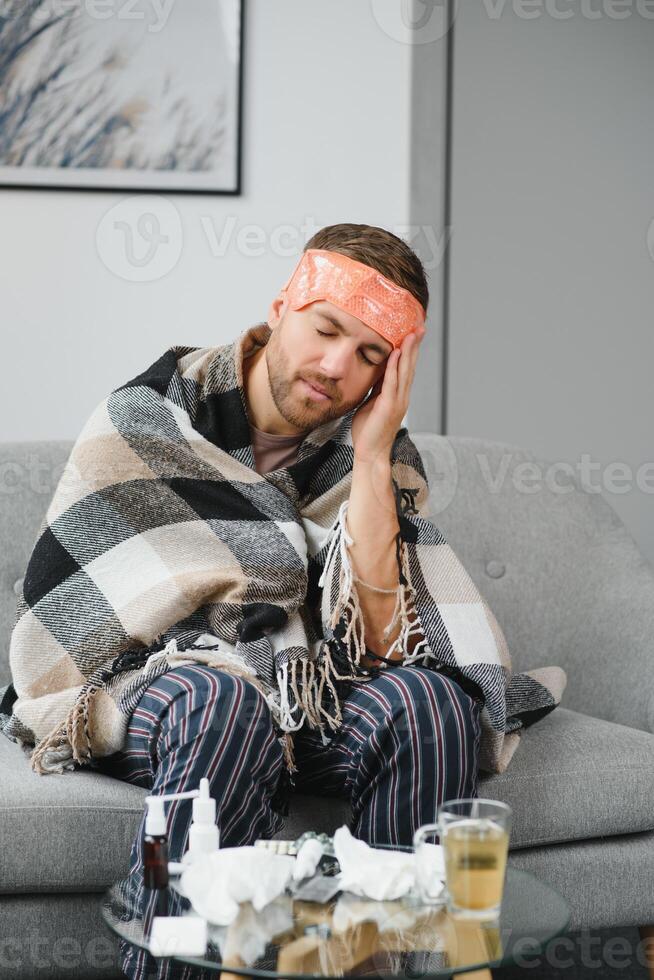 uma doente homem senta às casa em uma cinzento sofá com uma cobertor. doença, proteção, coronavírus, doença, gripe foto