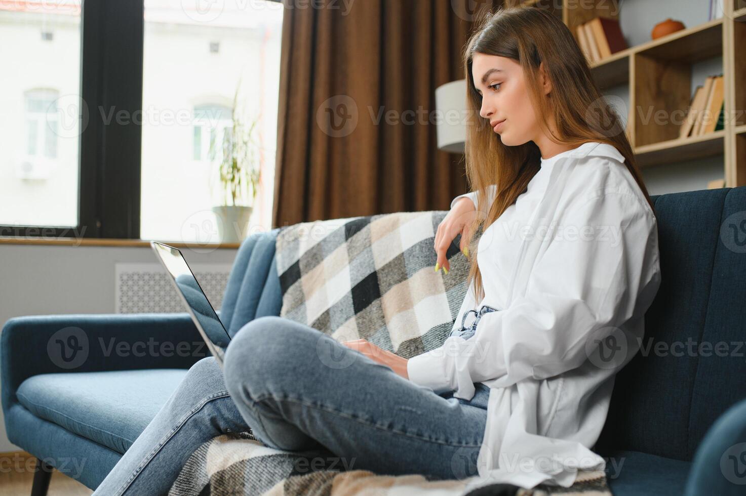 sorridente jovem mulher usando computador portátil, sentado em sofá às lar, lindo menina compras ou conversando conectados dentro social rede, tendo diversão, assistindo filme, trabalhador autonomo trabalhando em computador projeto. foto