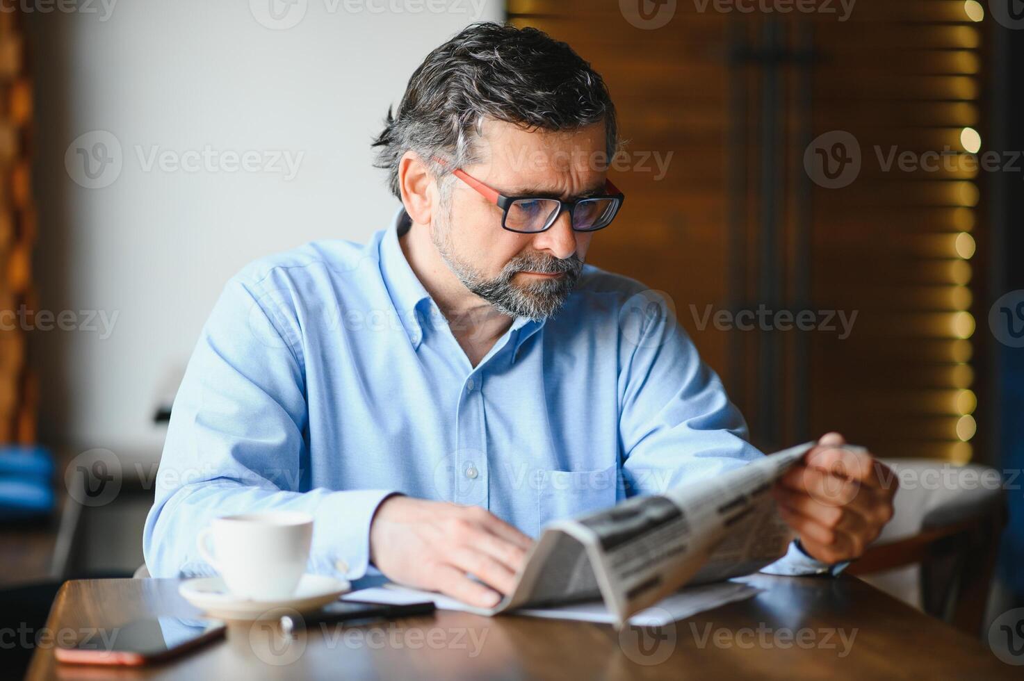 ativo Senior homem lendo jornal e bebendo café dentro restaurante foto