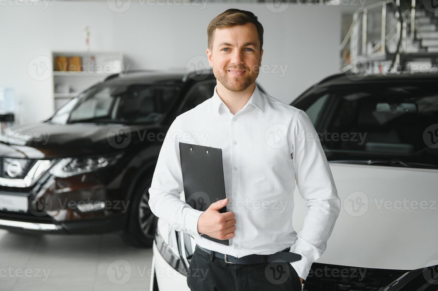 assistente dentro veículo procurar. retrato do uma bonito jovem carro vendas homem dentro roupa formal segurando uma prancheta e olhando às Câmera dentro uma carro concessionária foto