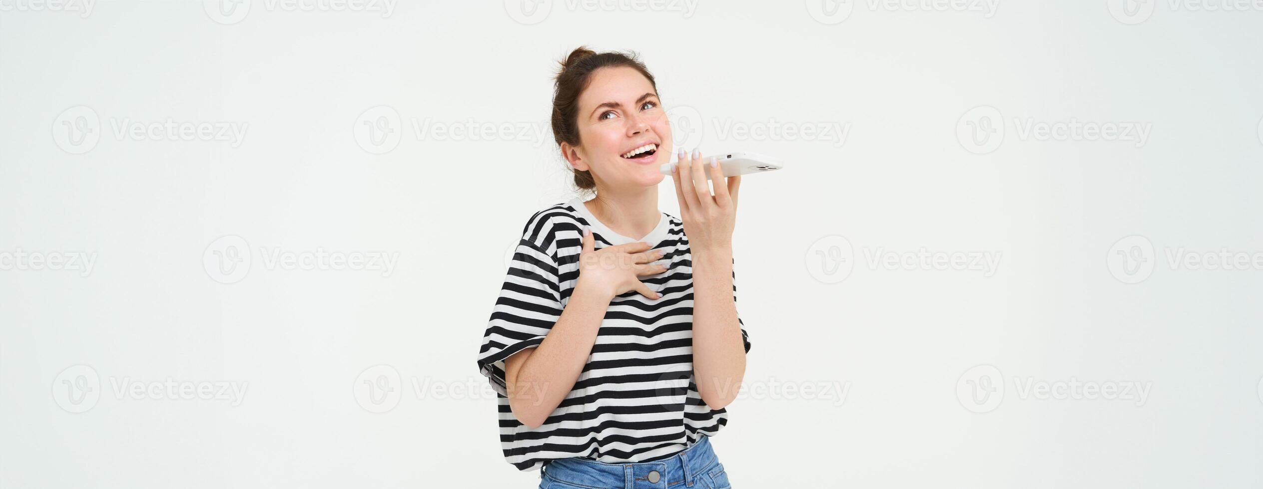 feliz jovem mulher explicando algo, usando Móvel telefone aplicativo, falando em viva voz, traduzindo dela voz, gravação uma mensagem, segurando Telefone perto lábios, branco fundo foto