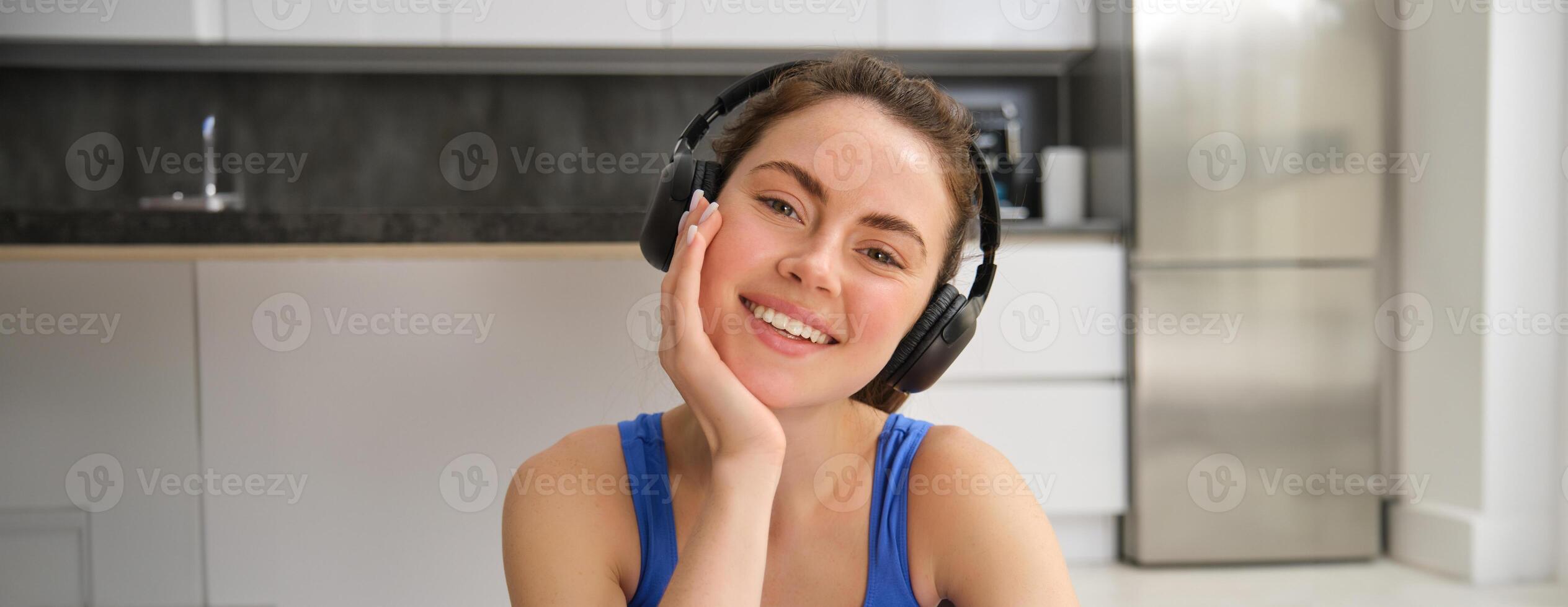 fechar acima retrato do lindo morena menina dentro roupa de esporte, senta dentro sem fio fones de ouvido e escuta música, enquanto fazendo exercite-se Treinamento às casa foto