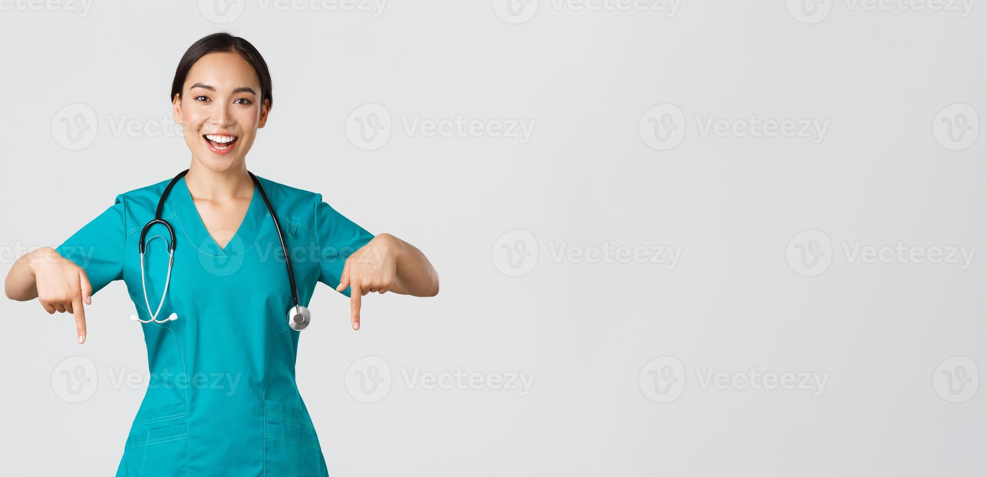 COVID-19, cuidados de saúde trabalhadores, pandemia conceito. feliz sorridente lindo ásia enfermeira, fêmea médico dentro esfrega apontando abaixo, convidativo para checar, mostrando hospital anúncio, branco fundo foto