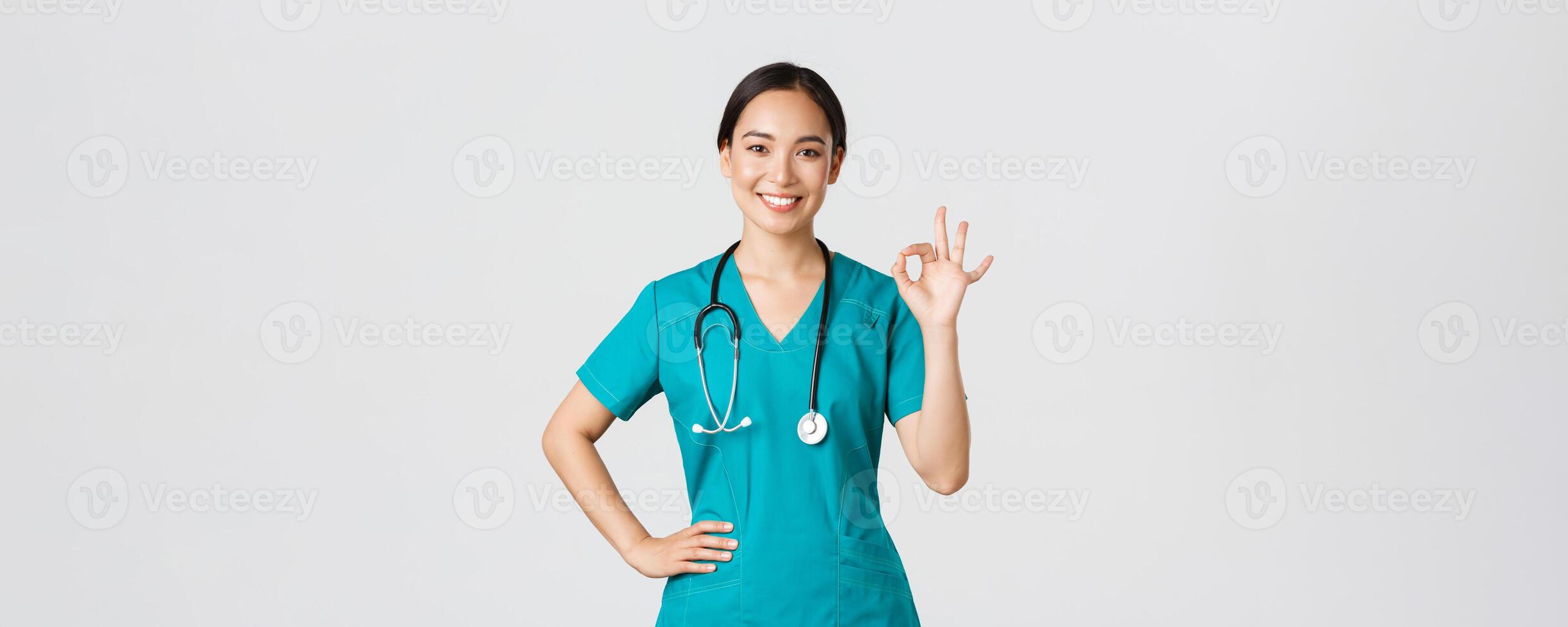 COVID-19, cuidados de saúde trabalhadores, pandemia conceito. profissional confiante sorridente ásia mulher doutor, fêmea enfermeira dentro esfrega assegurar tudo debaixo ao controle, mostrando OK gesto satisfeito foto
