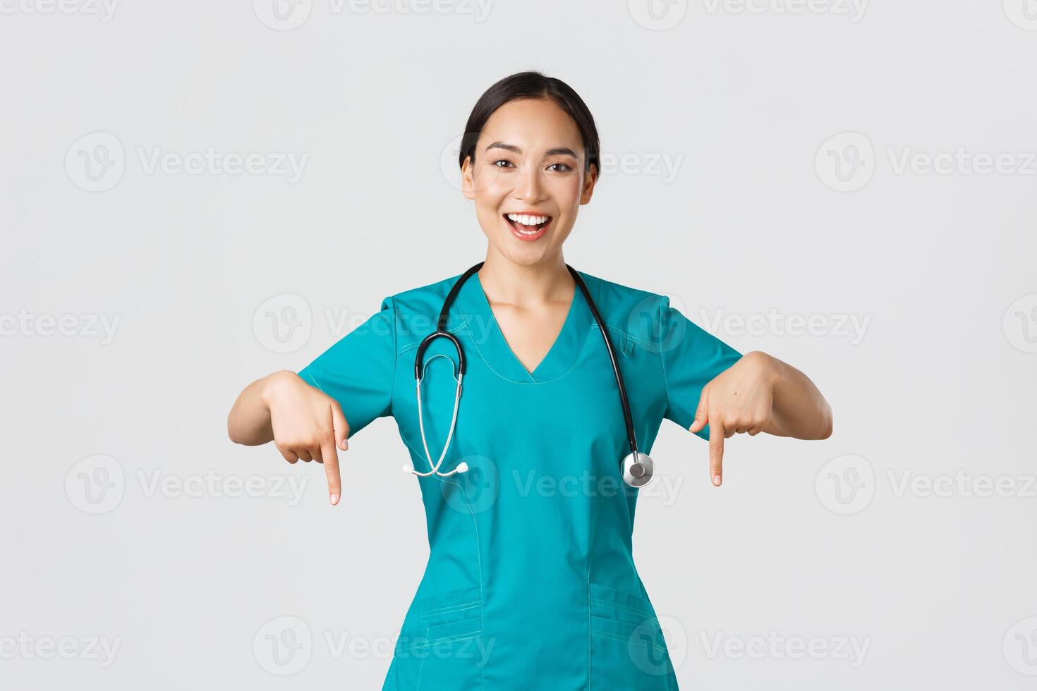 COVID-19, cuidados de saúde trabalhadores, pandemia conceito. feliz sorridente lindo ásia enfermeira, fêmea médico dentro esfrega apontando abaixo, convidativo para checar, mostrando hospital anúncio, branco fundo foto