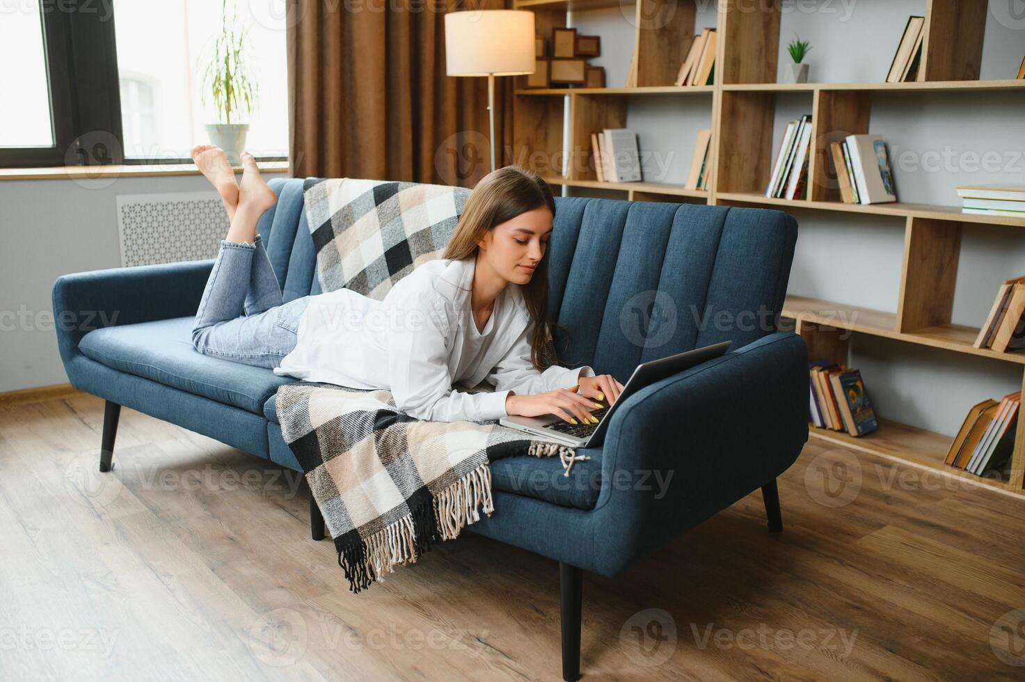 sorridente atraente jovem mulher sentado em sofá usando computador portátil comunicando trabalhando conectados às lar, feliz adolescente menina digitando em computador, desfrutando escrevendo blog ou conversando com amigos dentro social rede foto