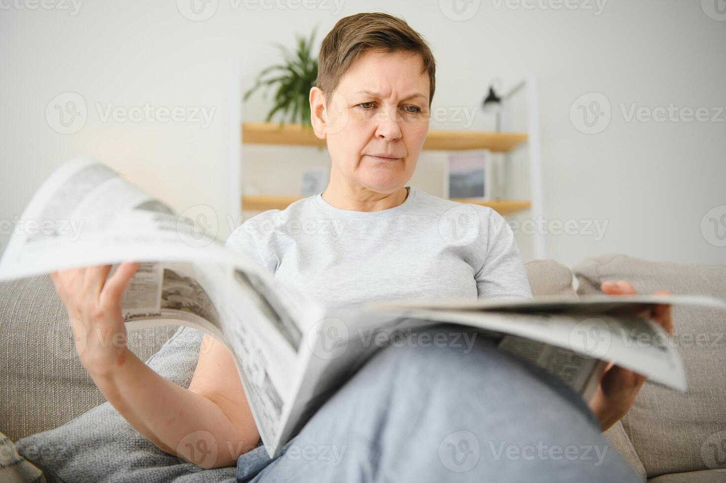 meio envelhecido mulher sentado sofá e lendo jornais. foto
