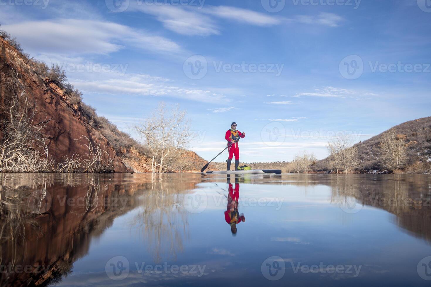 Senior remador dentro uma seco terno e vida Jaqueta é Treinamento em ficar de pé acima paddleboard em uma montanha lago dentro inverno condições - dente de cavalo reservatório dentro norte Colorado, baixo ângulo pov foto