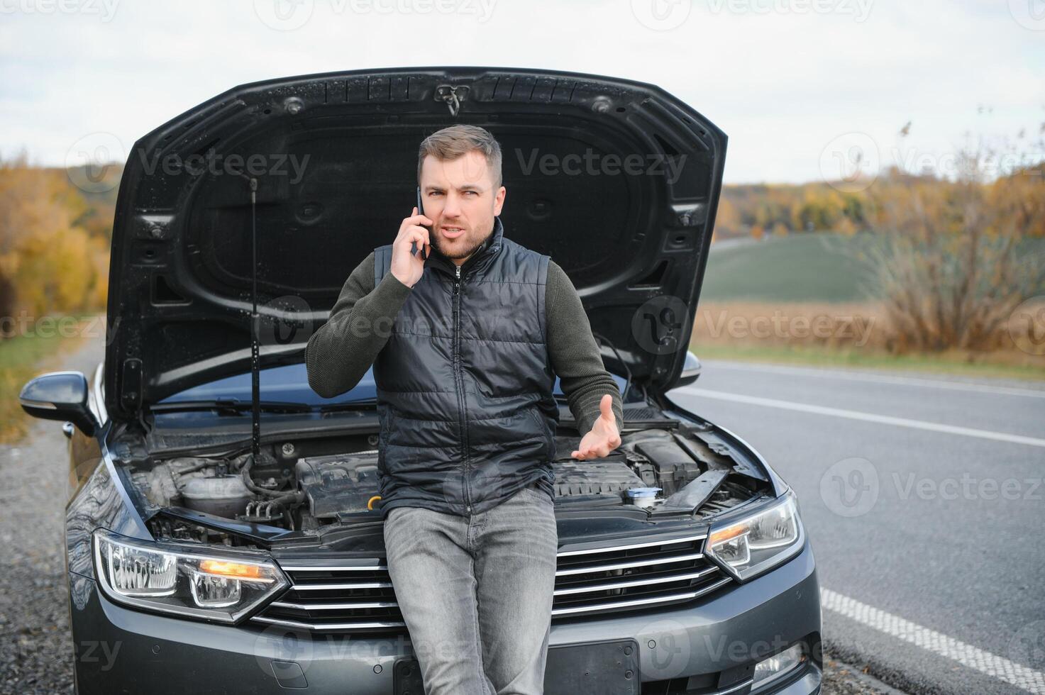 bonito jovem homem chamando para assistência com dele carro quebrado baixa de a beira da estrada foto