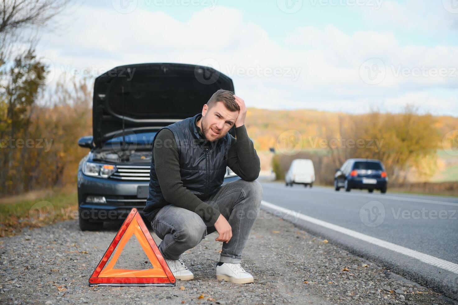 uma jovem homem com uma Preto carro este quebrou baixa em a estrada, cópia espaço. foto