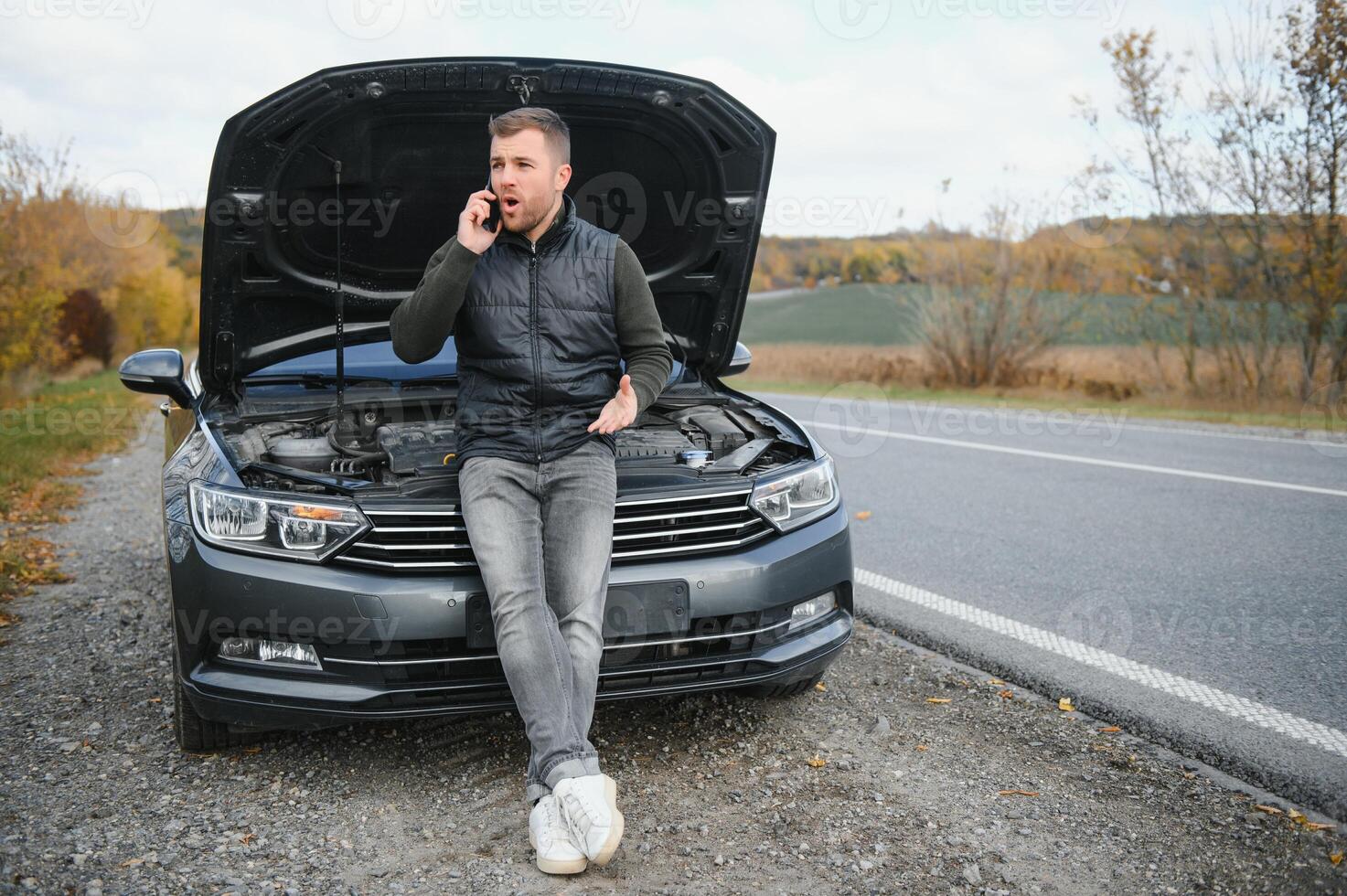 bonito jovem homem chamando para assistência com dele carro quebrado baixa de a beira da estrada foto