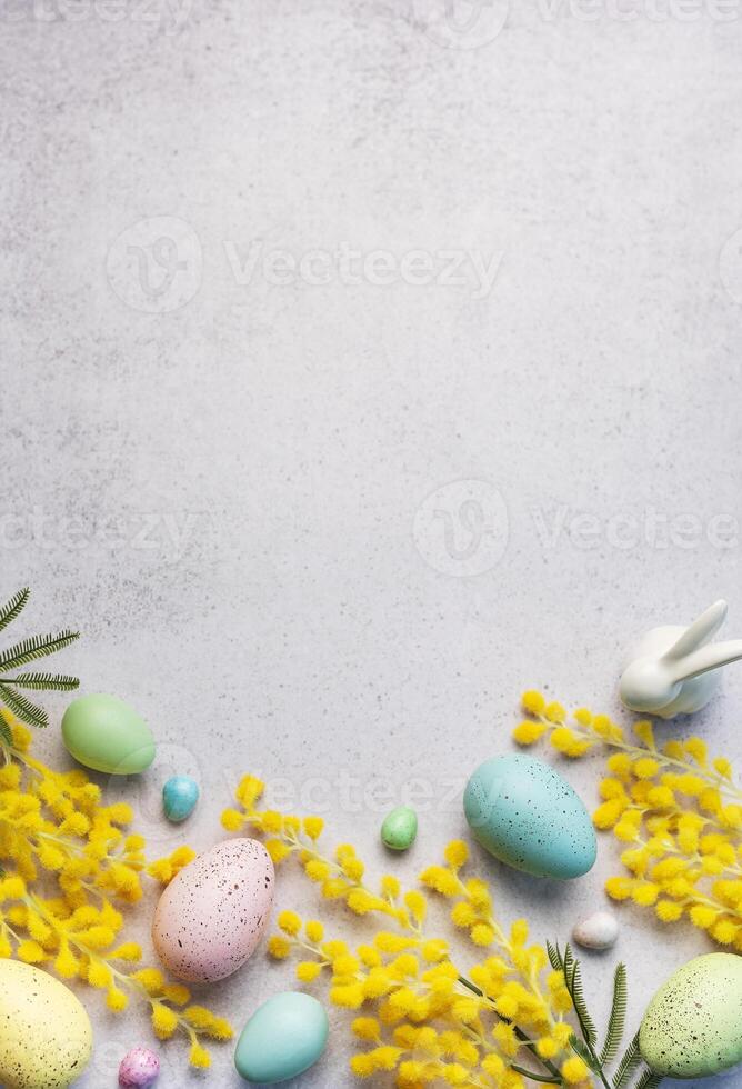 pastel Páscoa ovos e amarelo mimosa flores em uma luz cinzento fundo foto