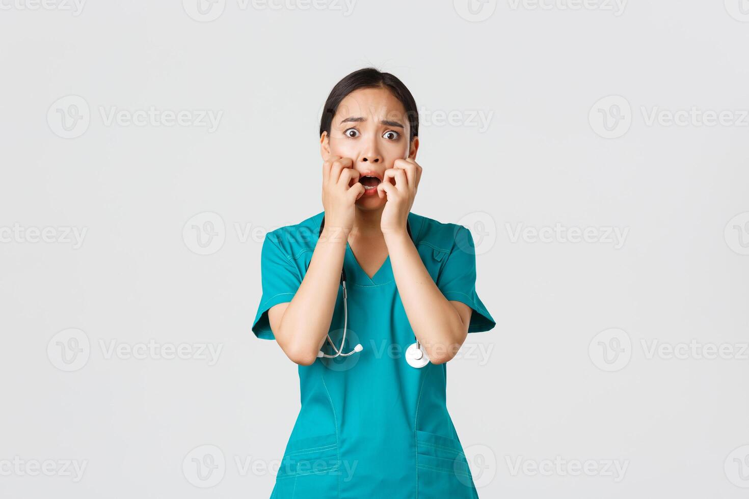 COVID-19, cuidados de saúde trabalhadores e impedindo vírus conceito. assustado inseguro ásia fêmea doutor, enfermeira dentro esfrega começa para pânico a partir de temer, morder unhas e olhando horrorizado, branco fundo foto