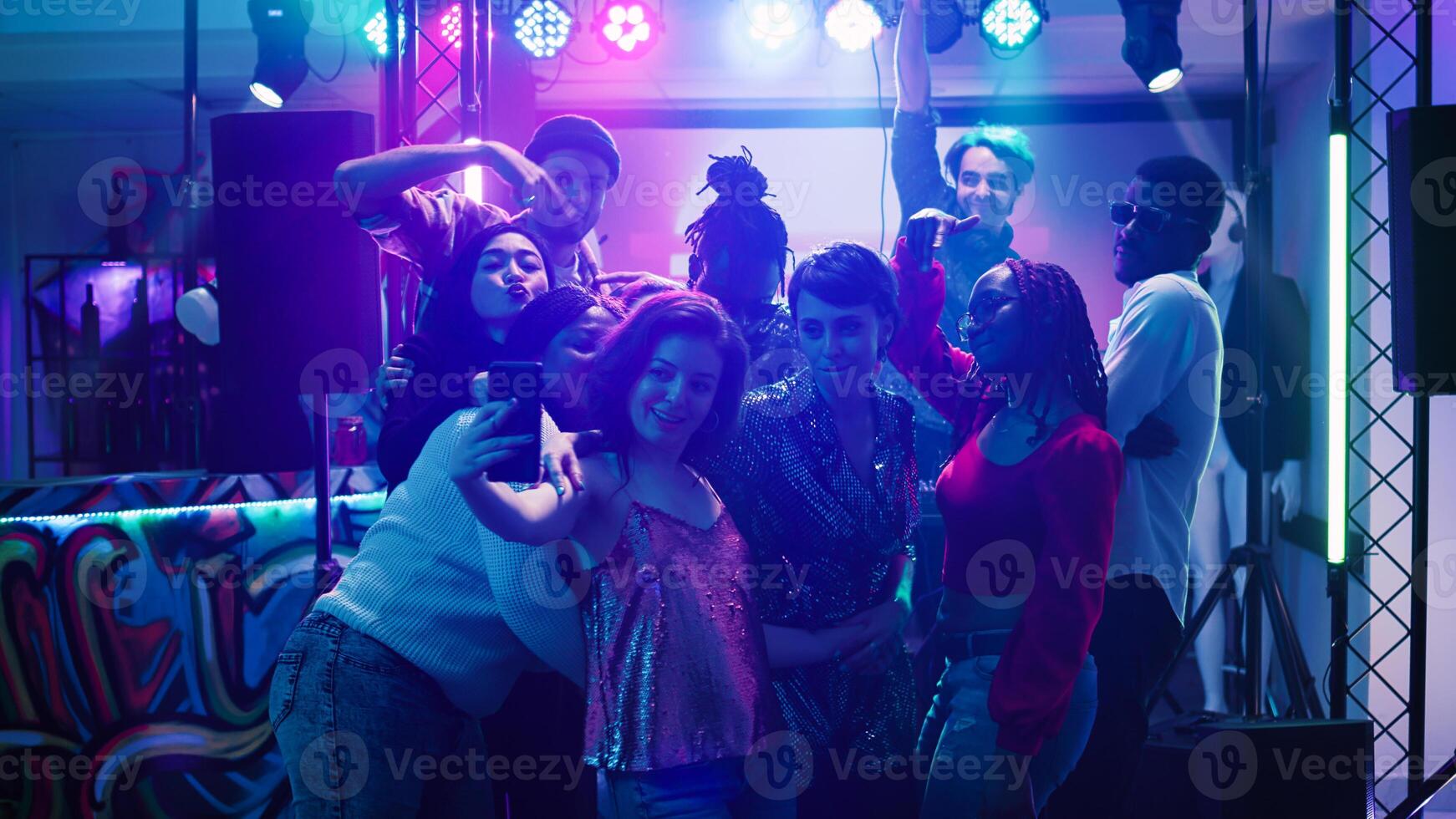 homens e mulheres levando fotos às festa e dançando juntos debaixo etapa luzes. jovem adultos tendo Diversão com As fotos em Smartphone, desfrutando discoteca evento às social reunião. portátil tomada.