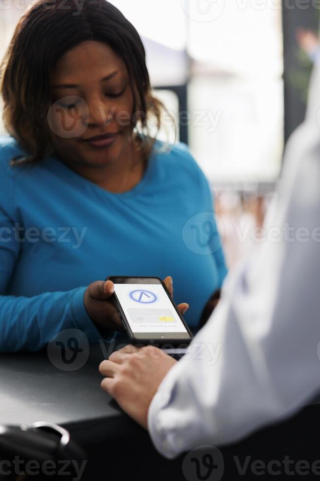 africano americano comprador comprando roupas com telefone nfc pagamento, usando Smartphone às pos terminal dentro moderno boutique loja. mulher pagando para elegante casual vestem e acessórios às contador. fechar acima. foto