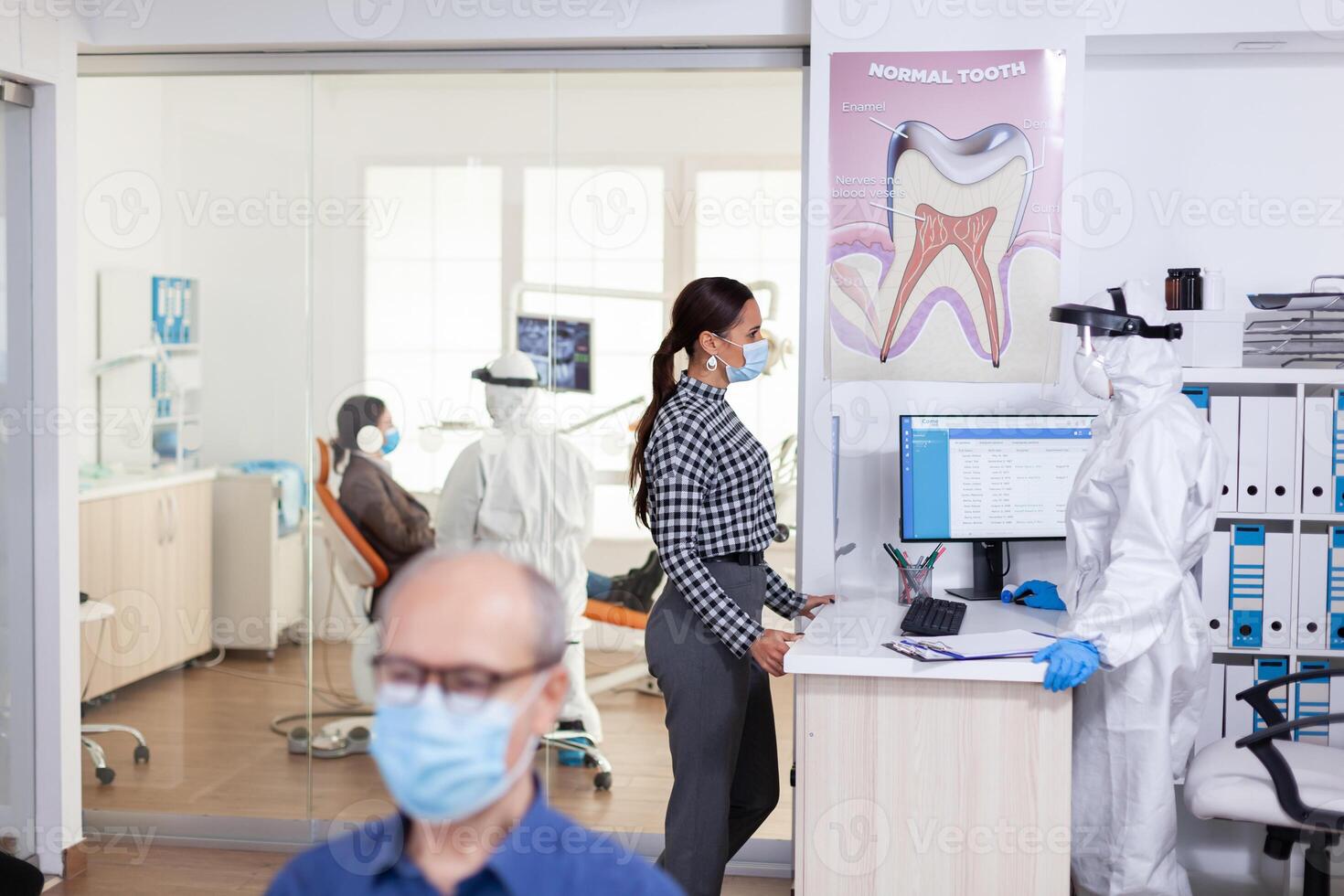 dentista enfermeira vestido dentro ppe terno com face shiled discutindo com paciente dentro estomatologia esperando sala. pessoas guardando social distanciar Como prevenção durante coronavírus surto. foto