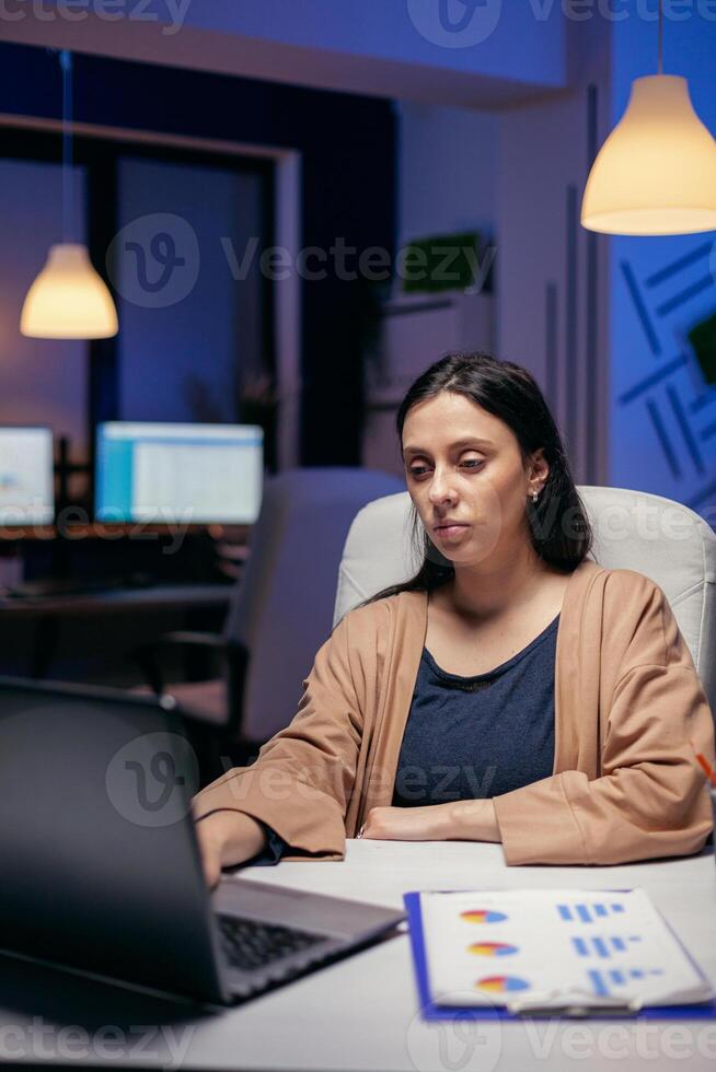 especializado empresária trabalhando em computador conectado para sem fio Internet acabamento uma mortal. inteligente mulher sentado às dela local de trabalho dentro a curso do atrasado noite horas fazendo dela trabalho. foto