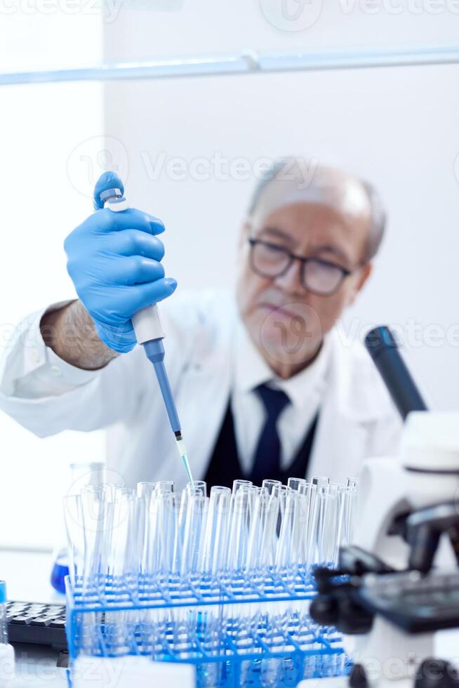 Senior farmacêutico cientista dentro moderno laboratório usando conta-gotas distribuidor com genético material. profissional químico usando pipeta com azul solução para microbiologia testes. foto