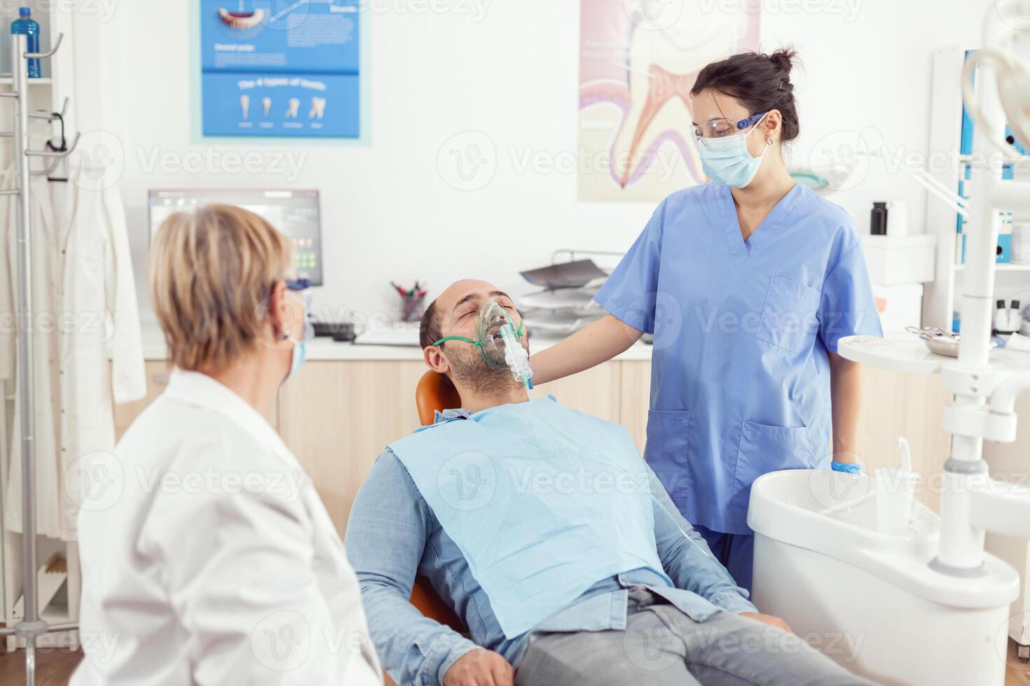 hospital assistente colocando oxigênio mascarar para doente homem paciente depois de estomatologia cirurgia, sentado em dental cadeira dentro ortodôntico hospital quarto durante médico consulta dentista médico examinando dor de dente foto