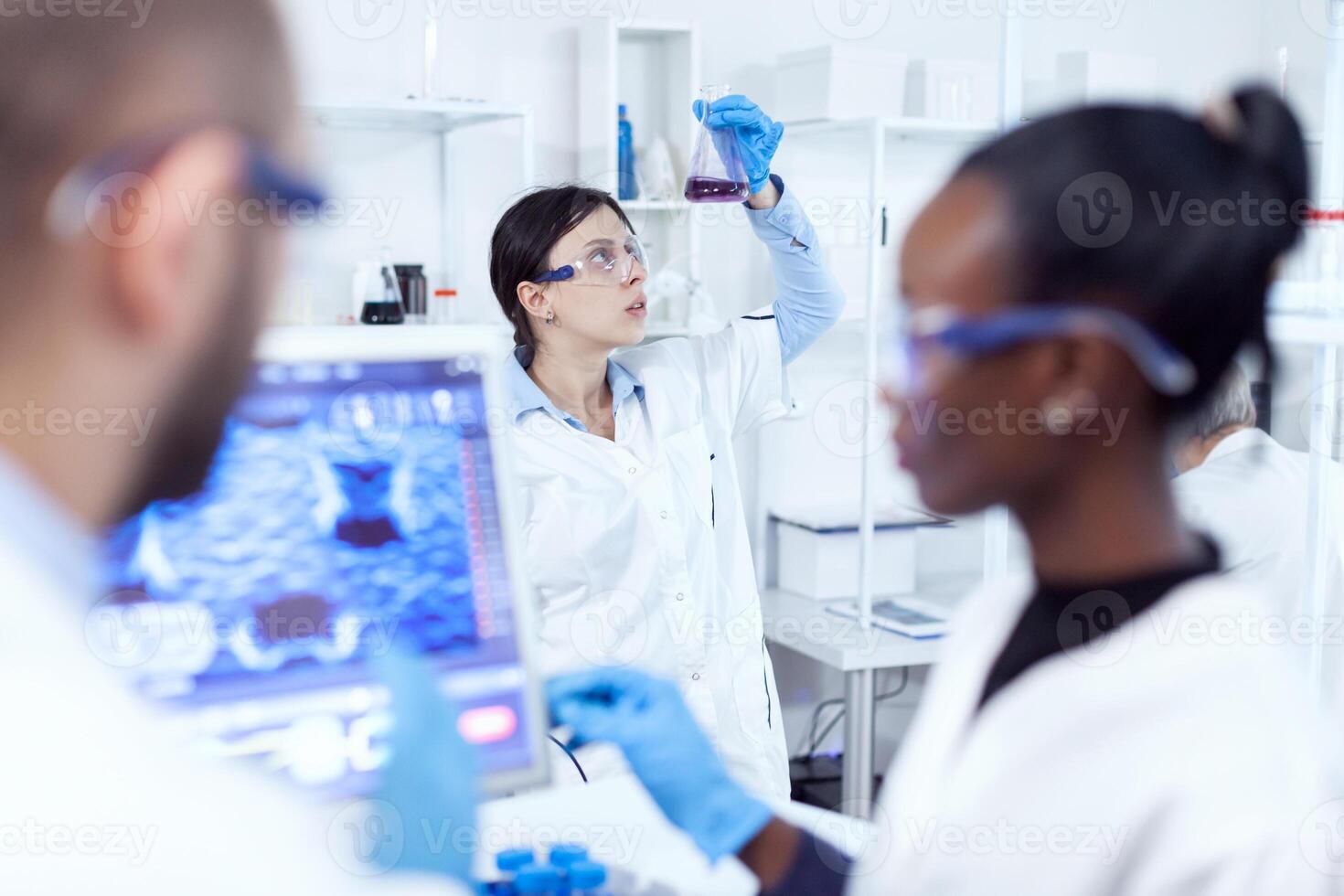 química especialista olhando às científico amostra dentro ocupado laboratório. multiétnico equipe do médico pesquisadores trabalhando juntos dentro estéril laboratório vestindo proteção óculos e luvas. foto