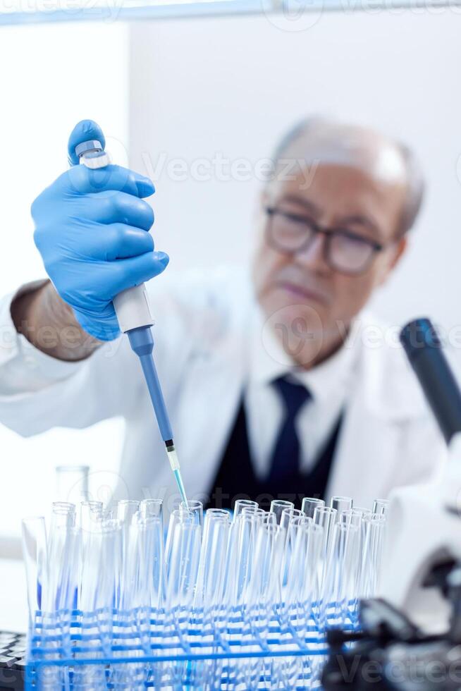 cientista com proteção engrenagem usando conta-gotas pipeta Engenharia vacina tratamento. Senior profissional químico usando pipeta com azul solução para microbiologia testes. foto