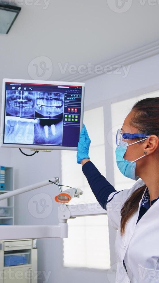 dentista médico e paciente olhando às digital tee raio X dentro dental escritório, pessoa pov. estomatologia vestindo protetora face mascarar e luvas apontando às dentes radiografia dentro estomatológico clínica foto