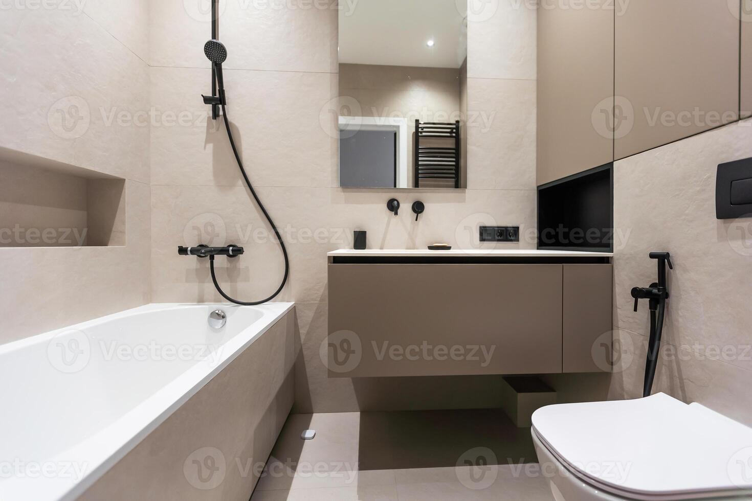 banheiro dentro uma moderno estilo com cinzento e branco azulejos. lá é uma ampla espelho com luminoso lâmpadas, de mesa com de madeira gavetas e afundar, banho com chuveiro e vidro partição, toalha prateleira e uma cabide. foto