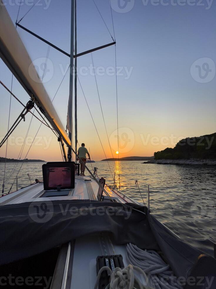 uma homem é em pé em a arco do uma barco a vela às pôr do sol foto