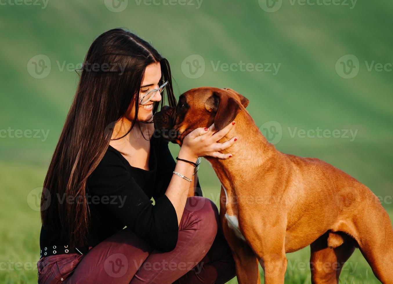 garota amando seu cachorro boxer no prado verde foto