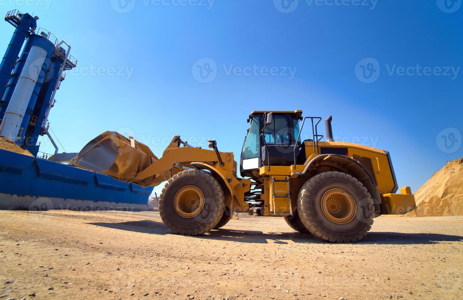 manutenção do amarelo escavadora em uma construção local contra azul céu. roda carregador dentro monte de areia fundo. seletivo foco. foto