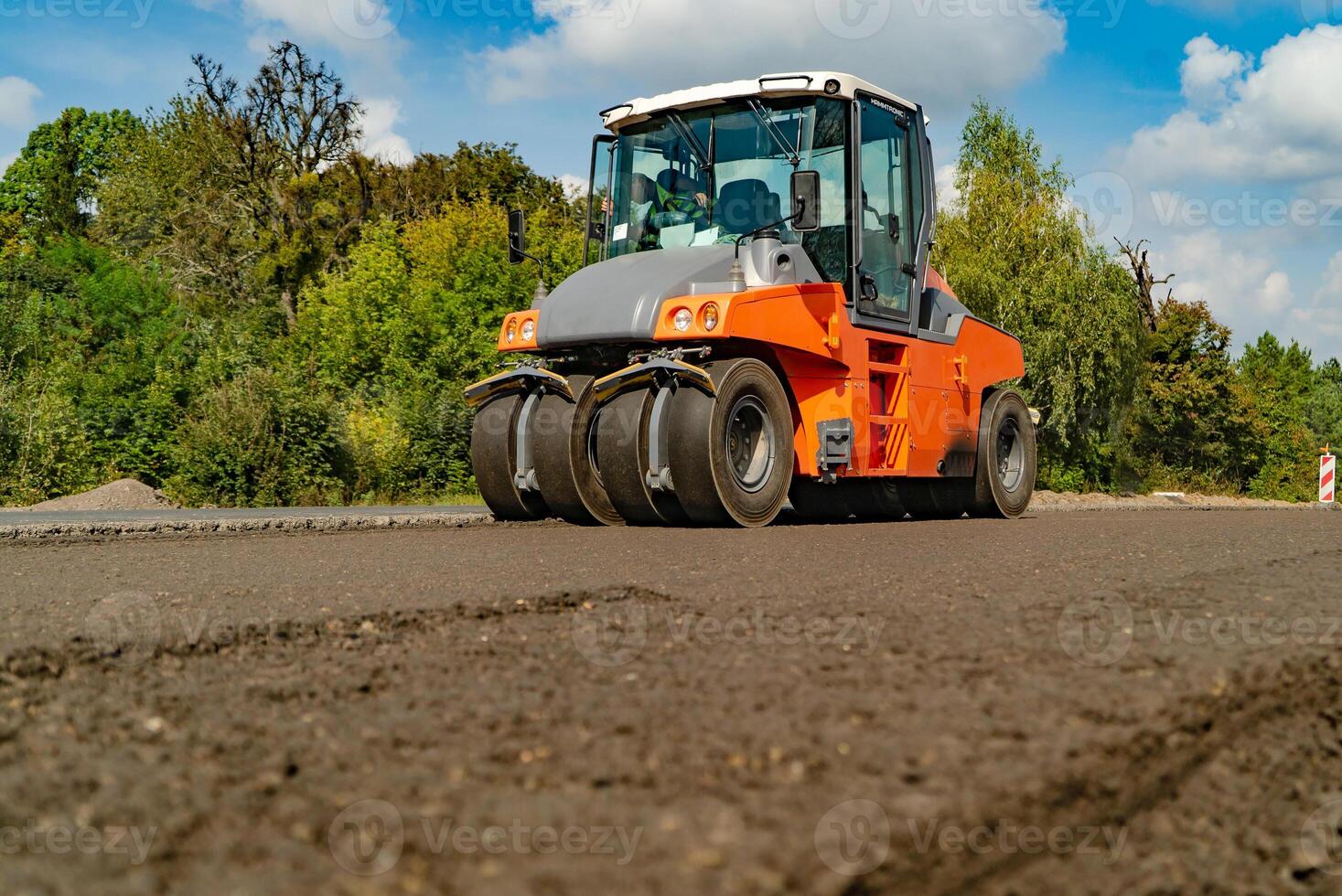 construção maquinaria para estrada trabalho passes através Novo asfalto dentro a verão em a fundo do árvores foto