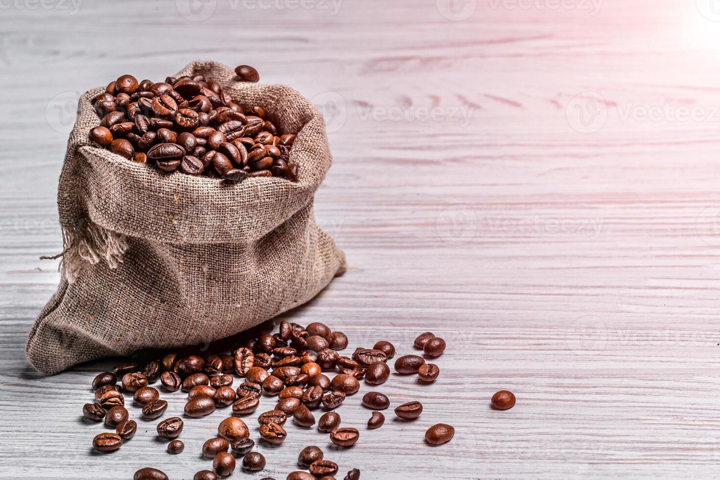 pequeno saco do café feijões e alguns grãos deitado perto isto em a luz fundo. café feijões espalhados perto a saco sobre a de madeira mesa. foto