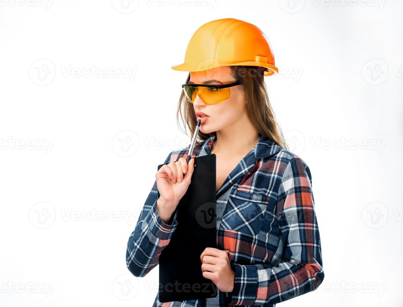 retrato do sério jovem mulher dentro capacete e segurança óculos tocante dela lábios com caneta e pensando isolado. fêmea arquiteto dentro capacete segurando Preto pasta e uma caneta olhando a parte, de lado foto