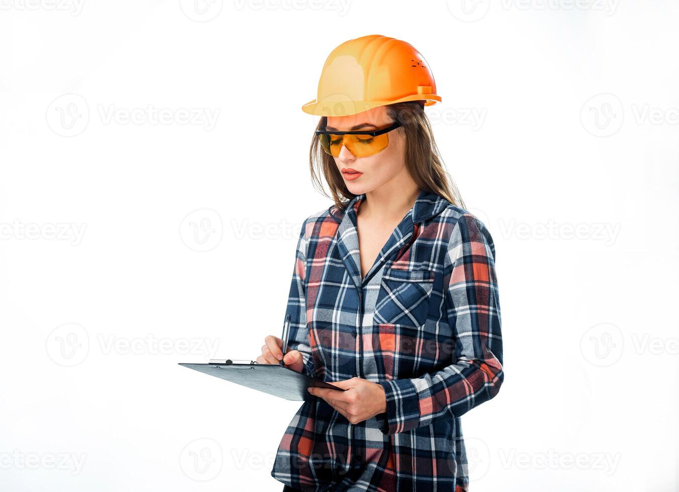 atraente mulher construtor dentro laranja capacete e protetora óculos com pasta dentro mão escrevendo em branco fundo. bonita engenheiro dentro camisa escrevendo com esferográfica caneta em Preto pasta foto
