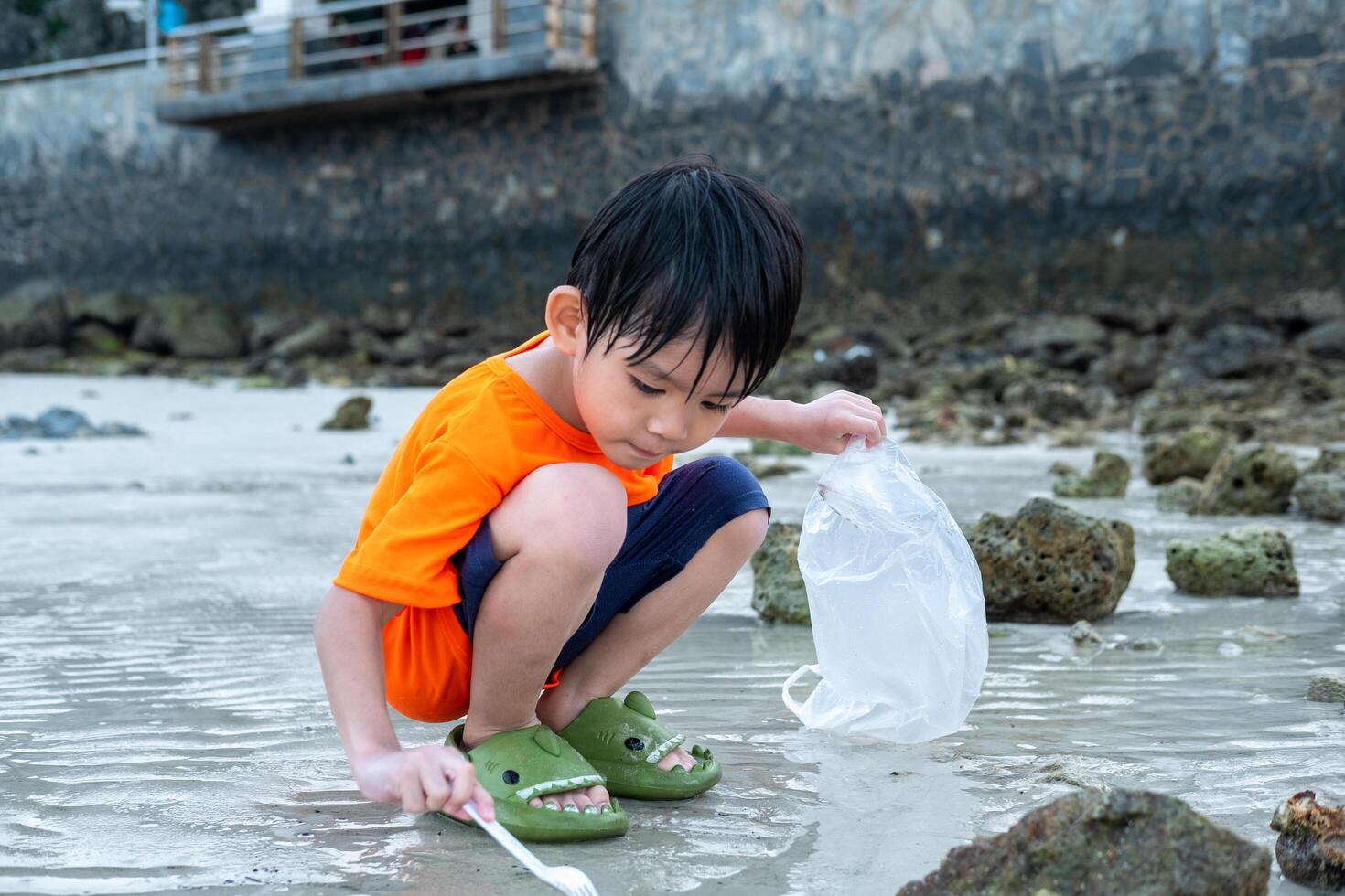 pequeno ásia Garoto ajuda escolher acima Lixo em a mar de praia. foto