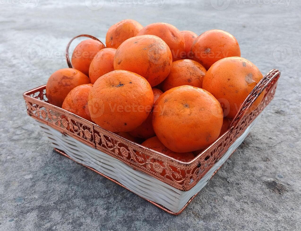 uma vime cesta cheio do fresco laranja frutas em a chão foto