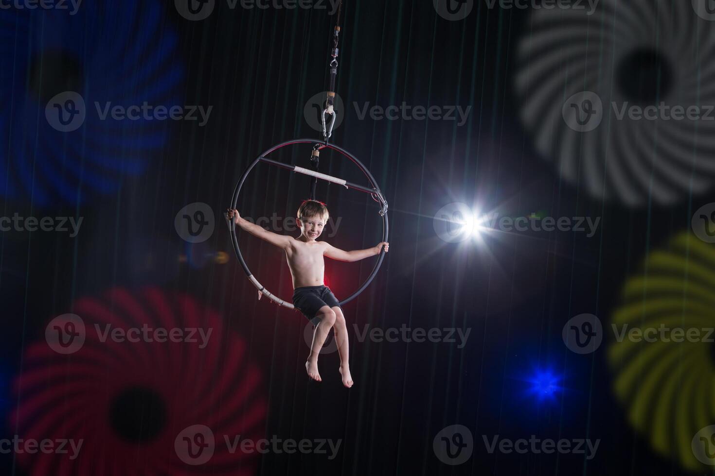 executa uma circo pequeno Garoto artista. circo aéreo ginasta em a aro. acrobacia. uma criança executa a acrobático truque dentro a ar foto