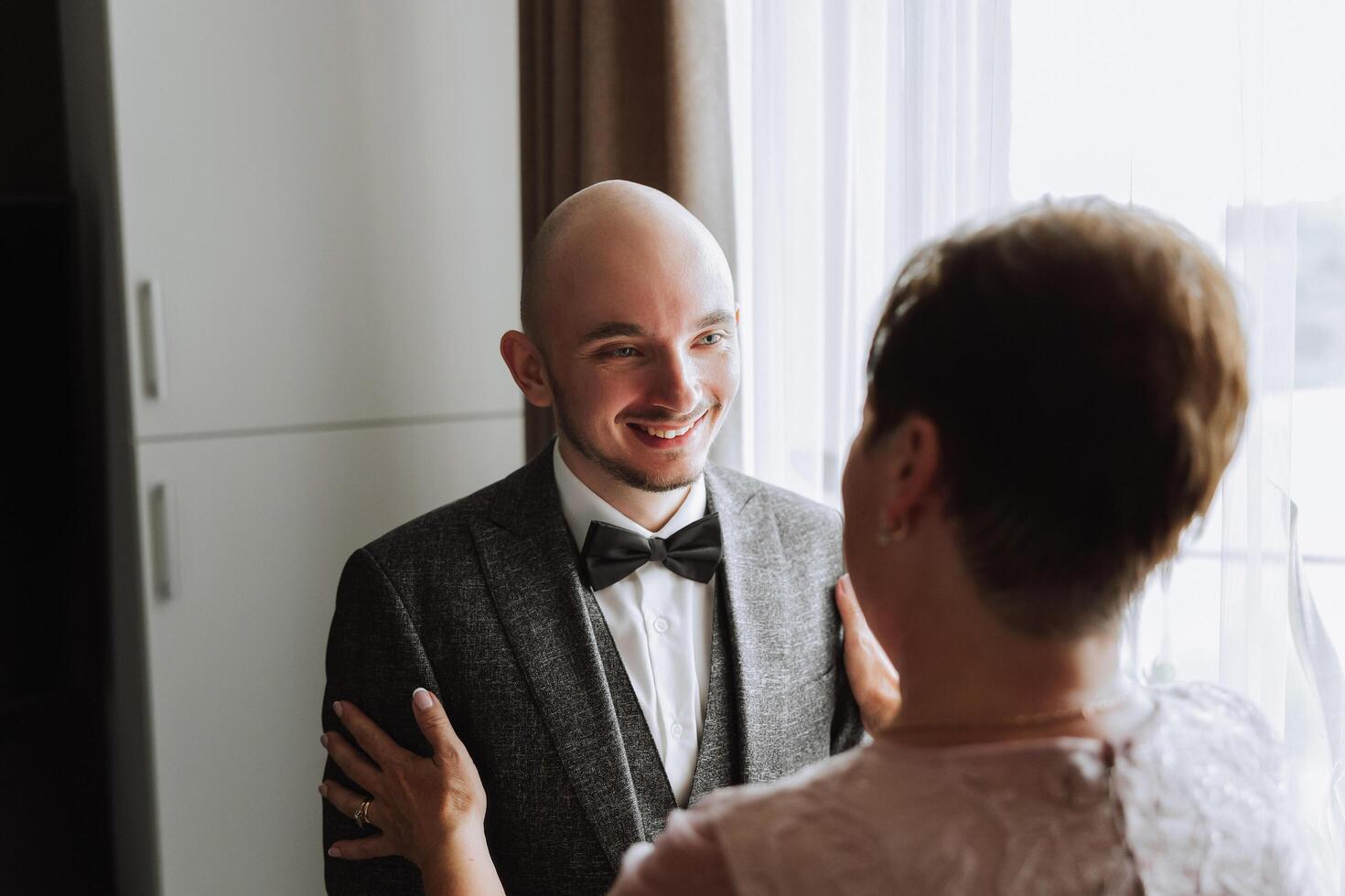 mãe ajuda dela adulto filho preparar para a Casamento cerimônia. a emocional e tocante momento às uma casamento. uma mãe abraços dela filho foto